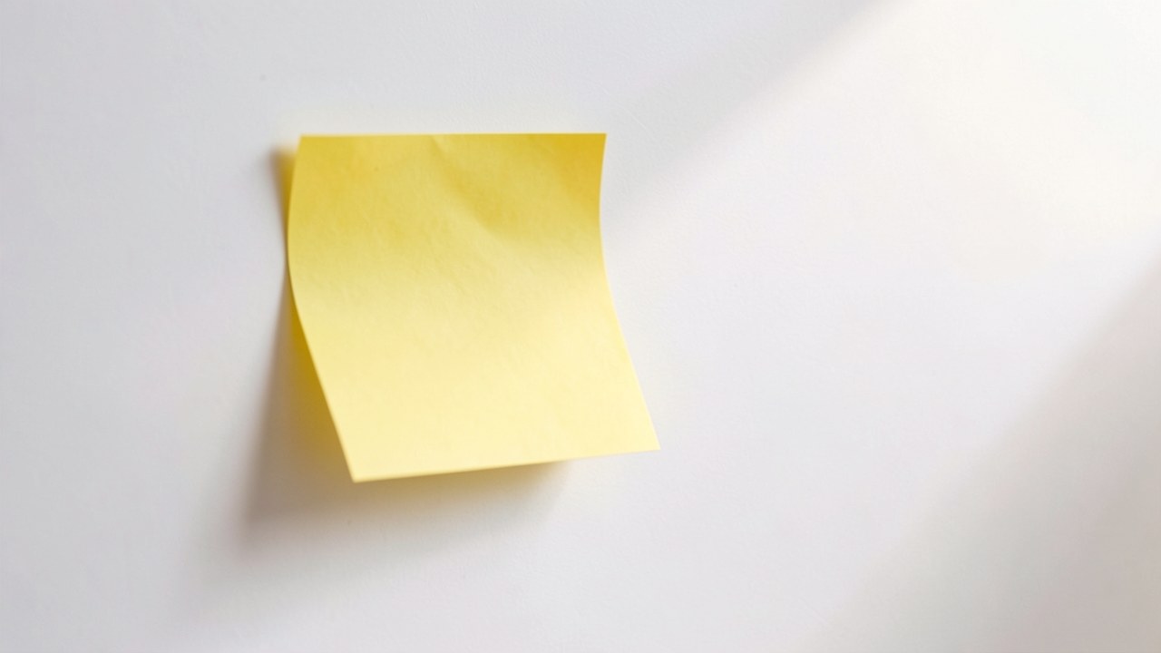 A yellow triangle-shaped sticky note is on a white wall, and the sticky note is empty, representing a caution message.